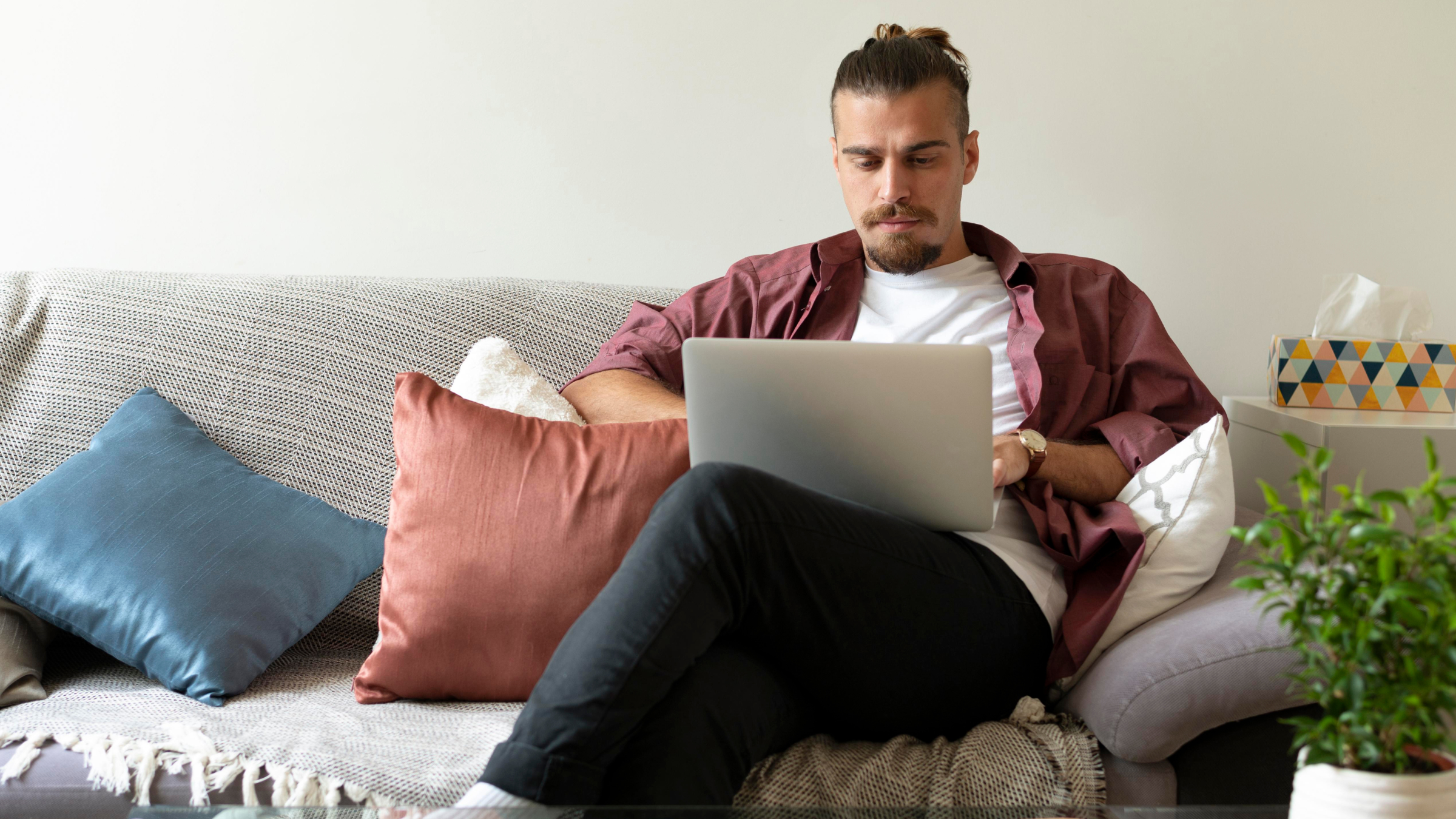 Man sitting on a sofa using a laptop to complete his HMRC self-employed registration online in the UK.