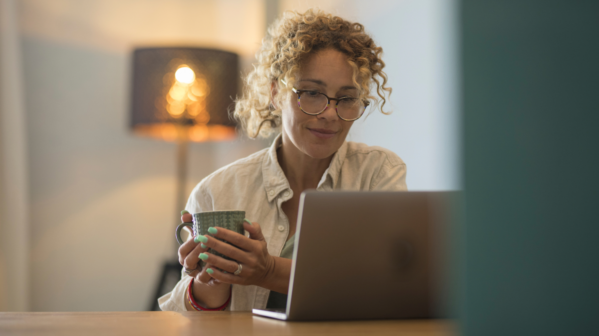 A self employed professional works on a laptop while holding a coffee mug in a comfortable home office, representing digital bookkeeping and preparation for a Making Tax Digital quarterly update.